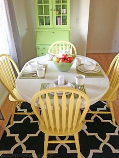 a dining room table with yellow chairs and green china cabinet in the backround