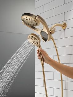 a person is holding the shower head and spraying it with their hands while standing in front of a white brick wall