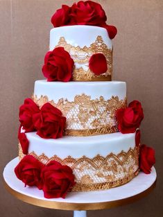 a three tiered cake with red roses on the top and gold trimmings