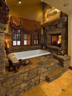 a bath tub sitting next to a fireplace in a room with stone walls and windows