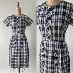 An adorable 1950s or early 1960s day dress! Made from black and white plaid cotton, the dress has a fitted bodice with short sleeves, a nipped waist, and a slim midi skirt. It features large black buttons down the front and down the side of the two large patch pockets on the front of the skirt. Unlined. Brand: illegible  Material: cotton  Estimated Size: Extra Small to Small (although the bodice unbuttons, there is no waist opening so the 30" waist must be slippe overhead)  Measurements: Shoulder: 13.5" Bust: 37" Waist: 30" Hip: 44" Length: 41" Bodice Length: 15.5" Condition: Great vintage condition! Some of the black areas have faded a bit to reveal the purples undertones. There are a few little pinholes and a faint spot on the skirt, as well as a small mend in at the corner of one pocket Vintage Plaid Dress For Work, Fitted Vintage Plaid Dress With Buttons, Fitted Plaid Dress With Buttons And Short Sleeves, Fitted Plaid Dress With Short Sleeves And Buttons, Vintage Plaid Short Sleeve Dress, Vintage Plaid Dress With Buttons, Vintage Short Sleeve Plaid Cotton Dress, Vintage Style Gingham Plaid Short Sleeve Dress, Vintage Gingham Plaid Dress With Short Sleeves