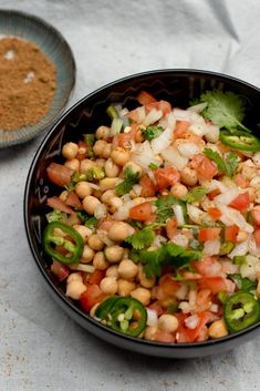 a black bowl filled with chickpeas salad next to a plate of seasoning