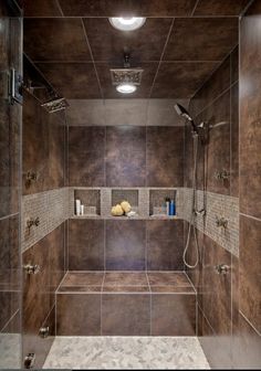 a walk in shower sitting next to a tiled wall and floor with brown tiles on the walls