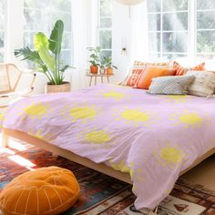 a bed with yellow and orange pillows on top of it next to a large potted plant