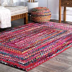 a multicolored rug in a living room next to a chair and table with pillows on it