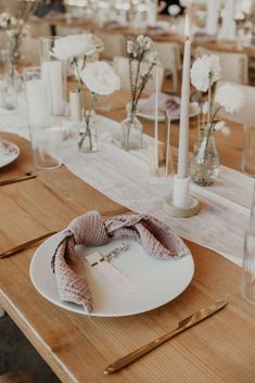 the table is set with white flowers, candles and napkins on top of it