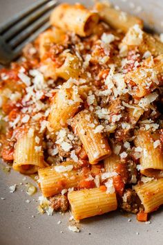 a plate full of pasta with meat and parmesan cheese on top, ready to be eaten