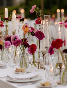 there are many vases with flowers and candles on the table