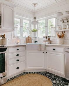 a kitchen with white cabinets and black and white floor tiles on the walls, an area rug in front of the sink