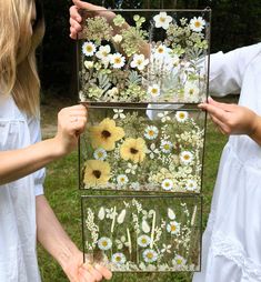 two girls are holding up an old window with flowers on it