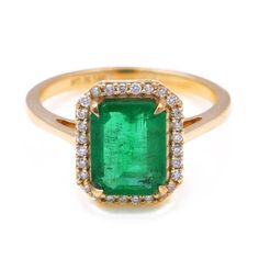 an emerald and diamond ring in yellow gold with diamonds around the band, on a white background