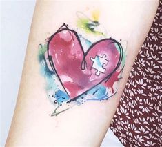 a watercolor tattoo with a heart and puzzle piece on the left side of the arm