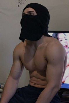 a shirtless man wearing a ski mask sitting in front of a tv