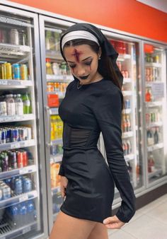 a woman in a black dress standing next to a refrigerator