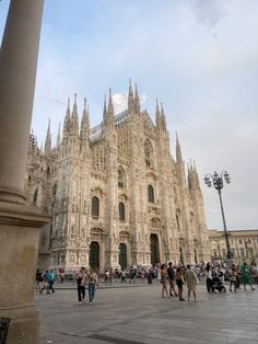 people are walking around in front of a large building with many spires on it