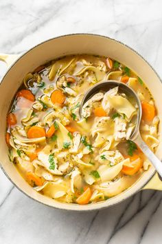 a pot filled with chicken noodle soup on top of a marble countertop next to a spoon