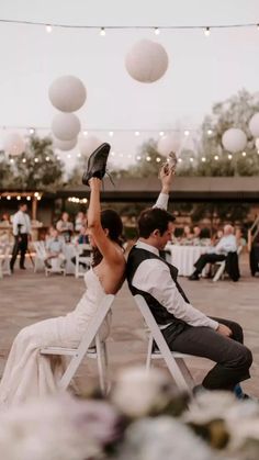 a bride and groom sitting on white chairs at their wedding reception with paper lanterns in the background