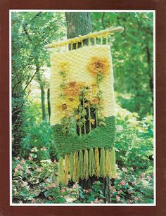 a crocheted blanket hanging from a tree in the woods with flowers on it