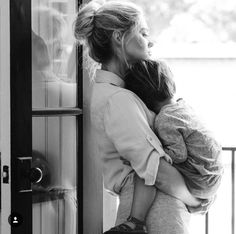 a woman holding a child in her arms while standing next to a door and looking out the window