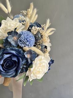 a bridal bouquet with blue and white flowers on display in front of a gray wall