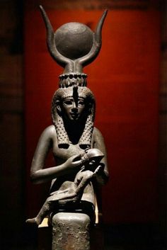 an ancient statue with horns on it's head sitting in front of a red wall