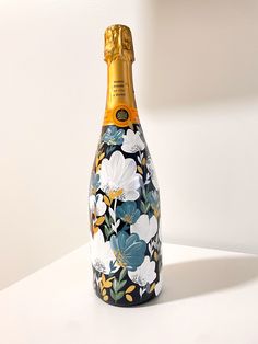 a bottle with flowers painted on it sitting on a white countertop next to a wall