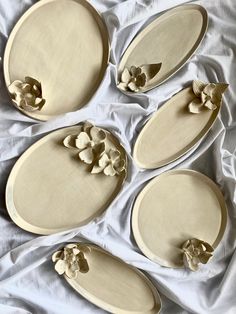 four oval trays with flowers on them sitting on a white cloth covered tablecloth