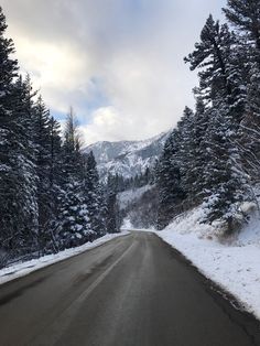 a snow covered road surrounded by trees and mountains