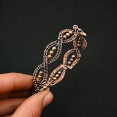 a hand holding a piece of metal wire with beads on it's end and an intricate design in the middle