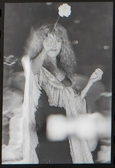 a black and white photo of a woman holding a flower in her hand while wearing a dress