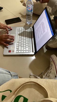 two people sitting at a table with laptops and water bottles in front of them