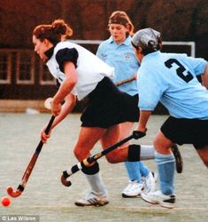 two girls playing field hockey on an asphalt court with the ball in front of them