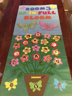 a bulletin board with flowers and butterflies in the center on a wooden table, along with a sign that says rooms is in full bloom