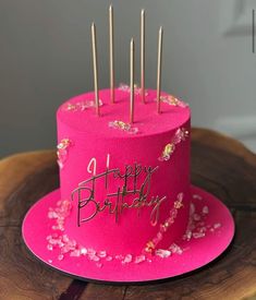 a pink birthday cake sitting on top of a wooden table