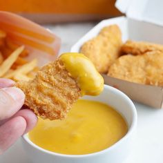 a person dipping some kind of food into a small white bowl filled with yellow sauce