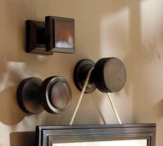 a mirror hanging on the side of a wall next to two wooden knobs and a rope