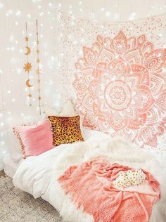 a white bed topped with pink pillows and blankets next to a wall covered in lights