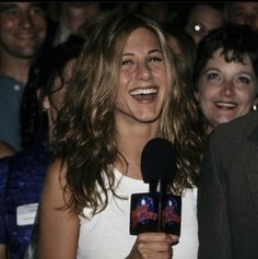 a smiling woman holding a microphone in front of a group of people at an event