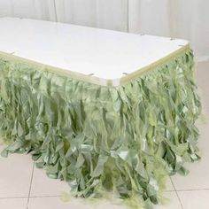 a white table topped with green leaves on top of a tile floor