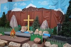 an outdoor setting with rocks, trees and a cross on the ground in front of a blue tarp