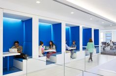 several people are sitting at desks in an office with blue walls and glass partitions