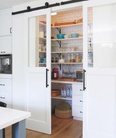 a kitchen with white cabinets and open doors to another room that has wooden flooring