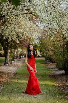 a woman in a red dress standing under some trees