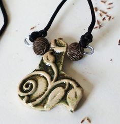 This pendant is designed with a flora and fauna motif making it a reversible necklace. The flora side displays leaves and vines. The pendant is cut to accent these. The reverse side or fauna gives the appearance of feathers or scales and forms a textured pattern. The color of the pendant is an antique gold with greenish patina. The cord is black poly satin. The two mesh antique gold beads are added as accents to the supporting nickel free wire. The pendant and beads measure approximately two(2) inches at the widest and also two(2) inches at the longest. The neck cord is a black satin poly blend and measures twenty-two(22) inches in length, letting the pendant rest at twenty-four(24) inches total. THIS IS A SLIP ON NECKLACE. NO DIFFICULT CLASPS. Adjustable Nature-inspired Necklace For Gift, Earthy Handmade Necklace For Gift, Nature-inspired Adjustable Pendant Necklaces, Adjustable Nature-inspired Pendant Necklaces, Artisan Jewelry With Adjustable Cord As Gift, Nature-inspired Jewelry With Adjustable Cord And Pendant, Nature-inspired Pendant Jewelry With Adjustable Cord, Ceramic Bead Jewelry, Crochet Hook Holder