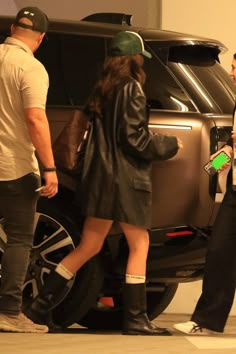 two men and a woman are standing in front of a car talking to each other