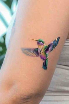 a small hummingbird tattoo on the right side of the arm, it is purple and green