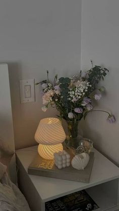 a vase with flowers on top of a table next to a book and lamp in the corner