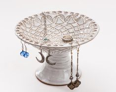 a white bowl with chains hanging from it's sides and two charms attached to the rim