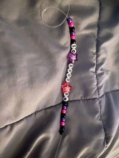 a purple and black beaded necklace on a silver satin sheet with pink stars hanging from it's end