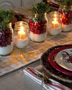 candles are lit in mason jars filled with berries and greenery on a dining room table